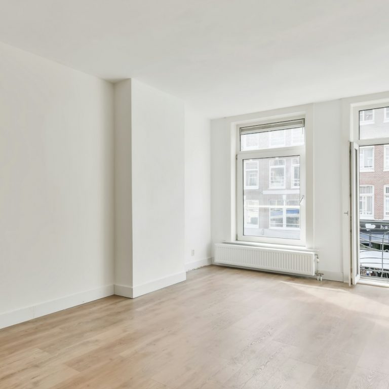 Interior shot of an empty room with white walls and a wooden floor with a balcony